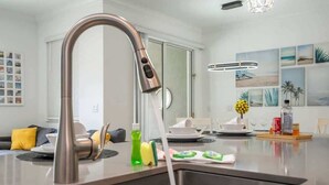 Eine moderne Küche mit Edelstahlarmatur, ein Essbereich mit Glastisch und ein Wohnzimmer mit Sofa und Kissen.