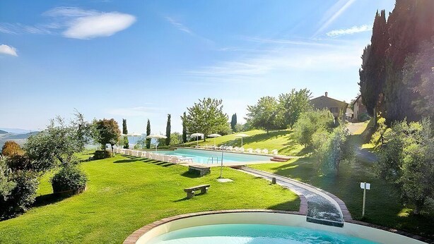 A swimming pool with a surrounding grassy area, benches, and a clear sky.