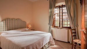 A bedroom with a bed, a nightstand, a lamp, a window with curtains, and a radiator.