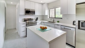 A modern kitchen with white cabinetry, stainless steel appliances, and a central island with fruit. - 5 Mi to Beach: Group Getaway w/ Yard in Miami (Miami)