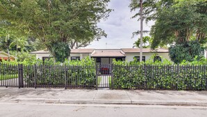 A gated residential area with a paved road, a metal fence, and lush greenery. - 5 Mi to Beach: Group Getaway w/ Yard in Miami (Miami)