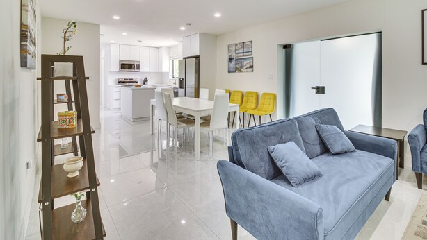 A modern living room with a blue sofa, a wooden shelf, and a dining area with yellow chairs. - 5 Mi to Beach: Group Getaway w/ Yard in Miami (Miami)
