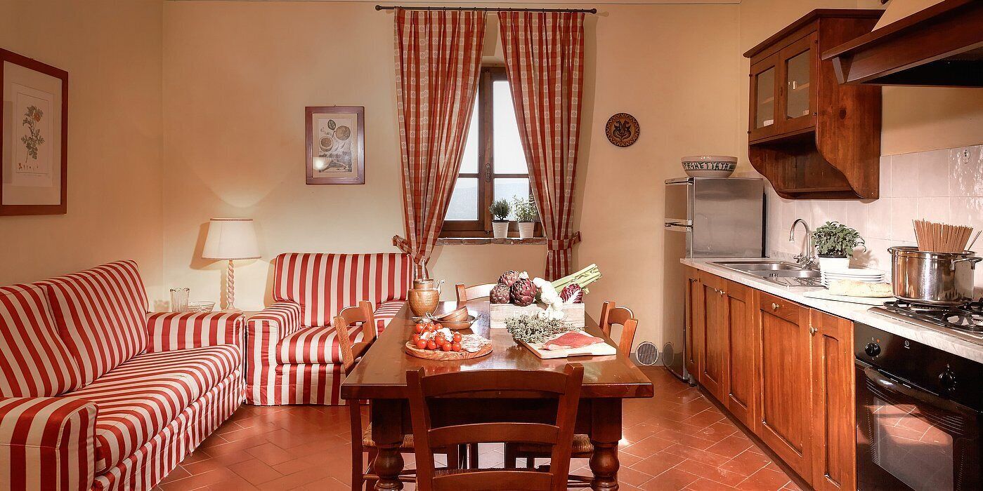 Una sala de estar acogedora con un sofá a rayas, una mesa de comedor con una bandeja de frutas y una cocina con armarios de madera y una estufa.