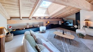 Une chambre mansardée chaleureuse avec une lucarne, un canapé, une table basse et un téléviseur.