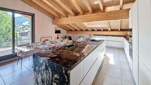 Une cuisine moderne dotée d’un grand îlot central, de poutres en bois au plafond et offrant une vue sur un paysage verdoyant.