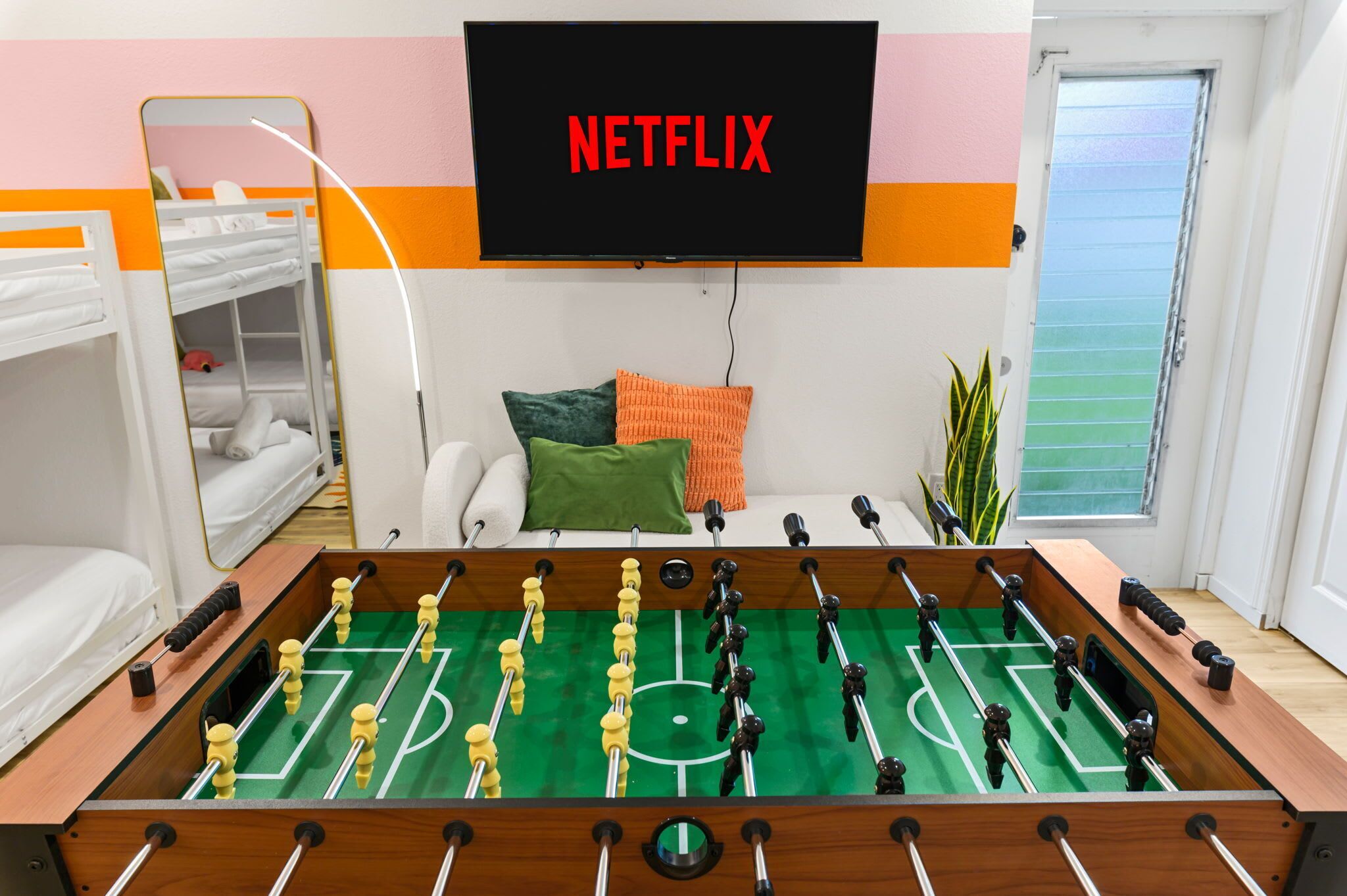 A room with a foosball table, bunk beds, a TV displaying 'NETFLIX', and a window with a view.