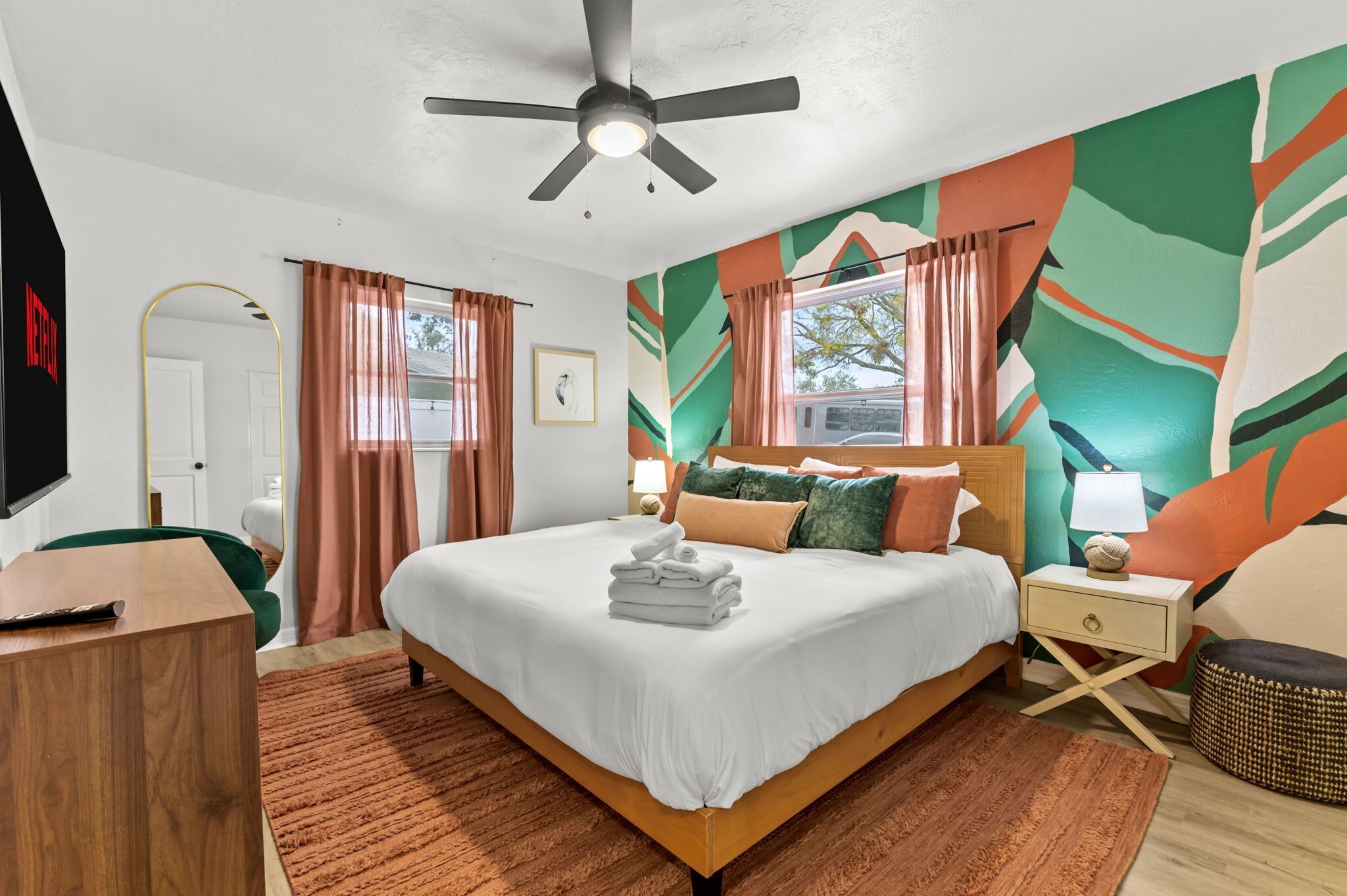 A modern hotel room with a large bed, a ceiling fan, a TV, and a window with curtains.
