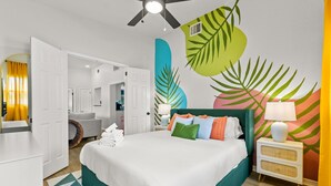 A modern hotel room with a large bed, a ceiling fan, and a vibrant tropical mural on the wall. - Gulf Coast Getaway | Pool, Putting Green & Pickleball (Seminole)
