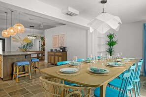A dining area with a wooden table set for six, blue chairs, and a bar area with wicker stools.
