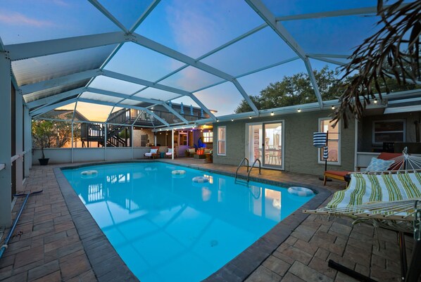 An indoor swimming pool with a covered patio area, a lounge chair, and a small table.
