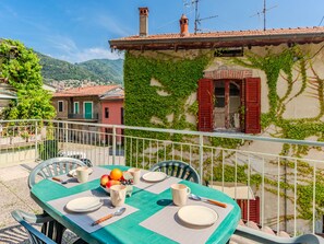 A dining table set outdoors with a view of a building covered in ivy and a red-roofed structure in the background.