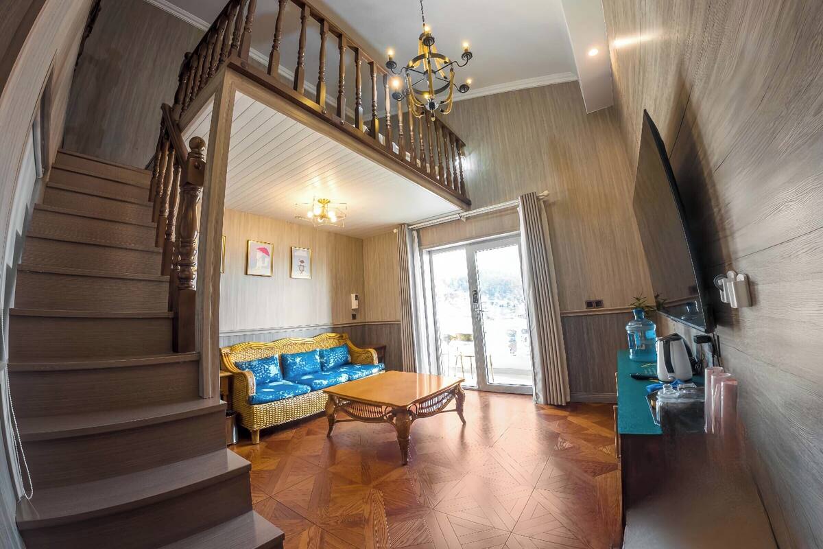 A spacious living area with a wooden staircase, a blue sofa, a wooden coffee table, and a chandelier.