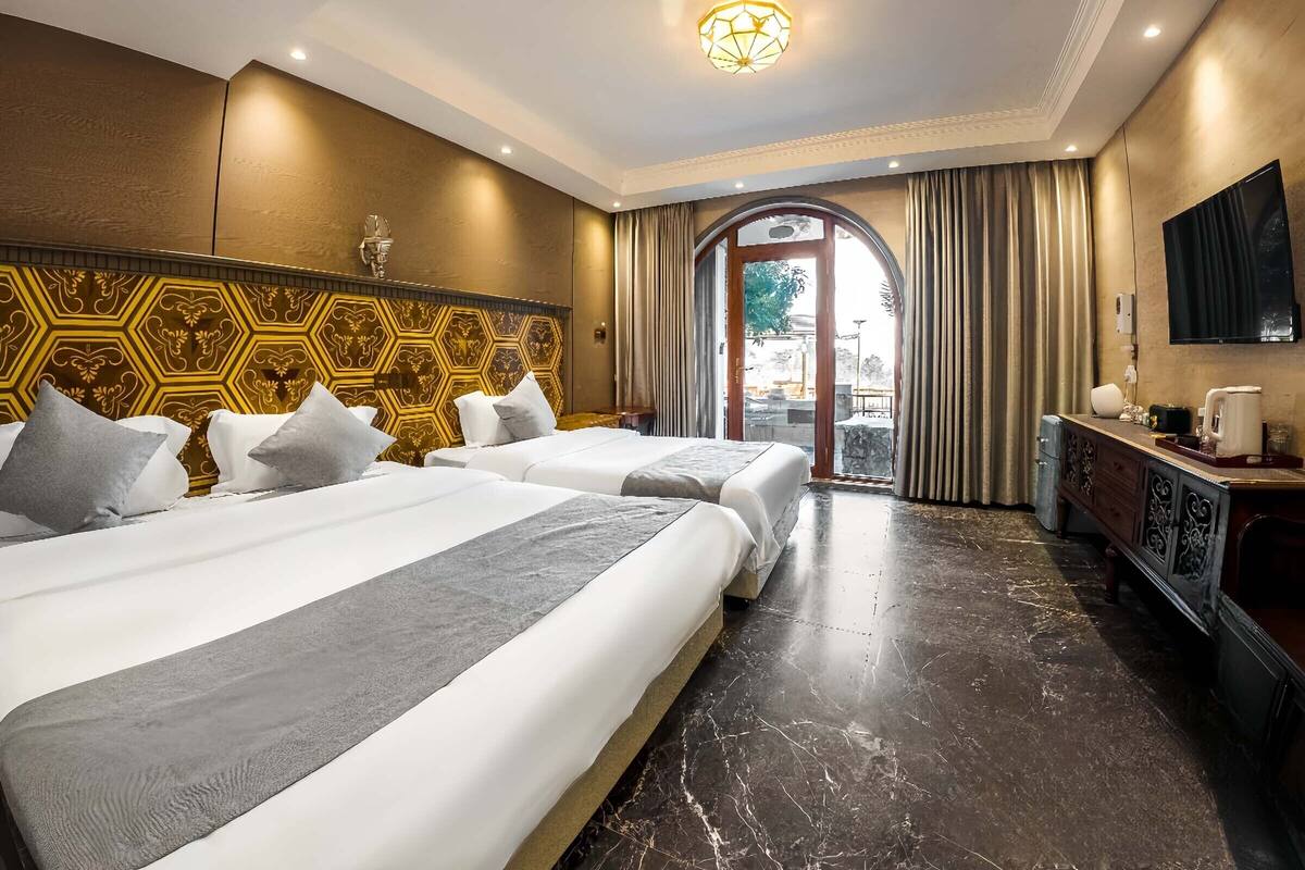 A hotel room with two beds, a TV, a desk, and a view through a doorway.