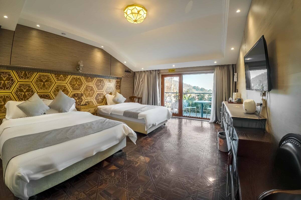 A hotel room with two beds, a TV, a desk, and a balcony with a view.