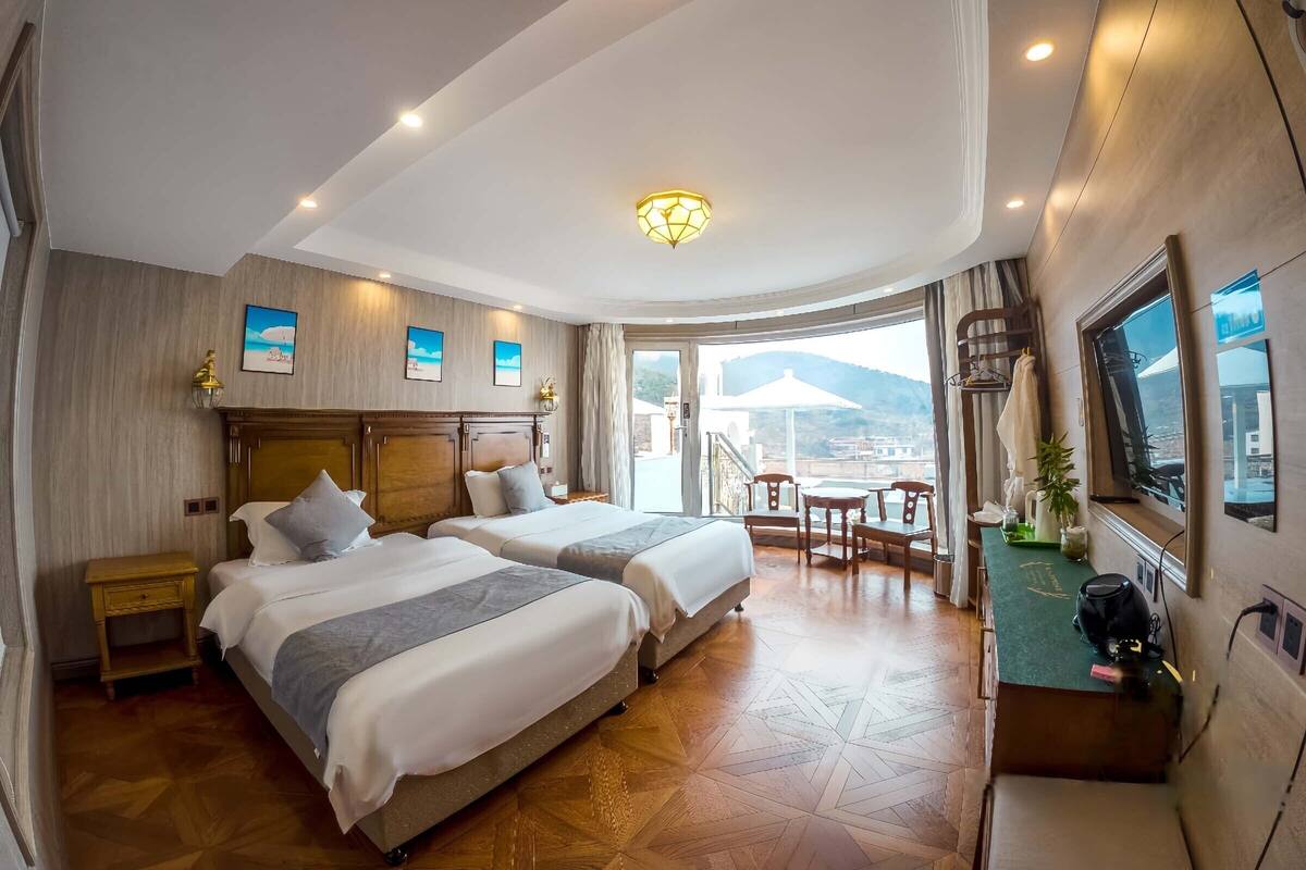 A hotel room with two beds, a balcony with a table and chairs, and a view of the mountains.