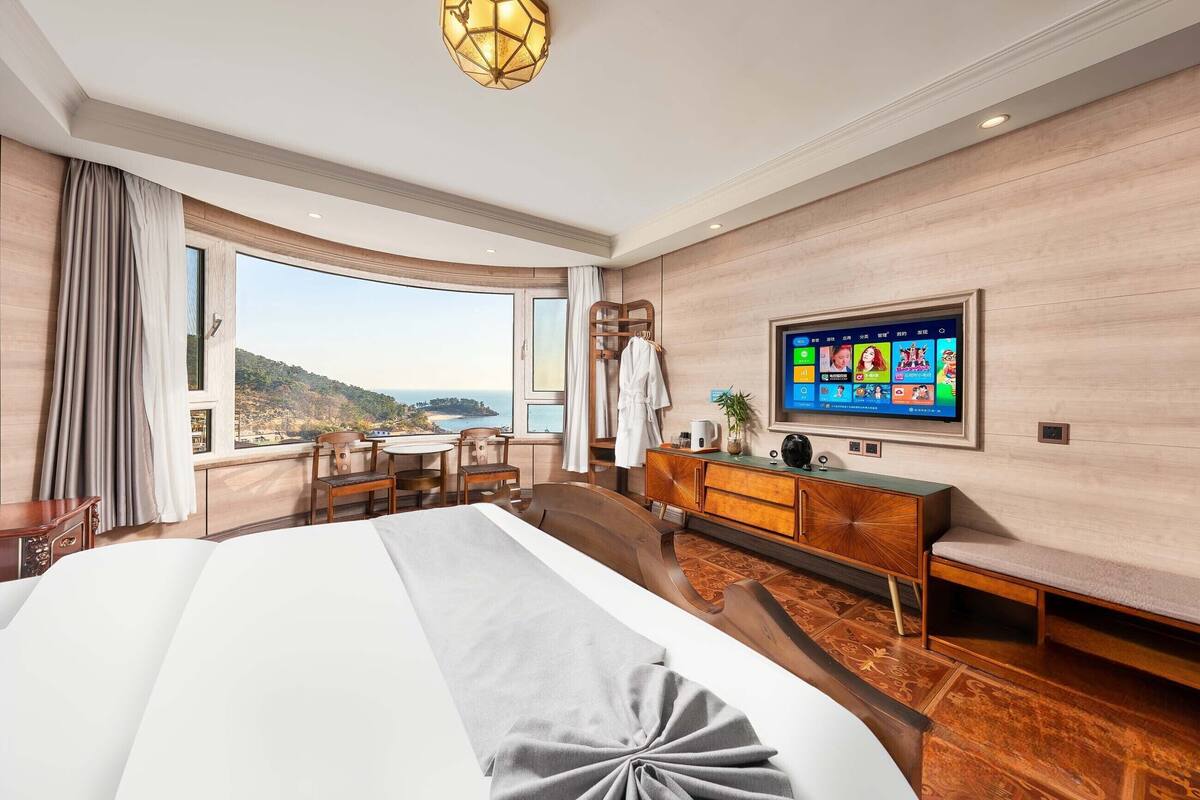 A hotel room with a large bed, a desk, a TV, and a view of the outdoors.