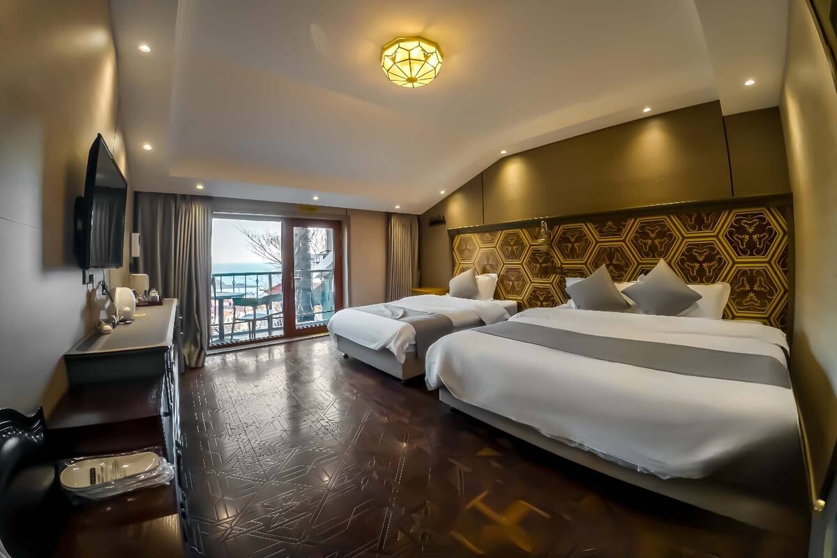 A hotel room with two beds, a desk, a TV, and a balcony with a view.