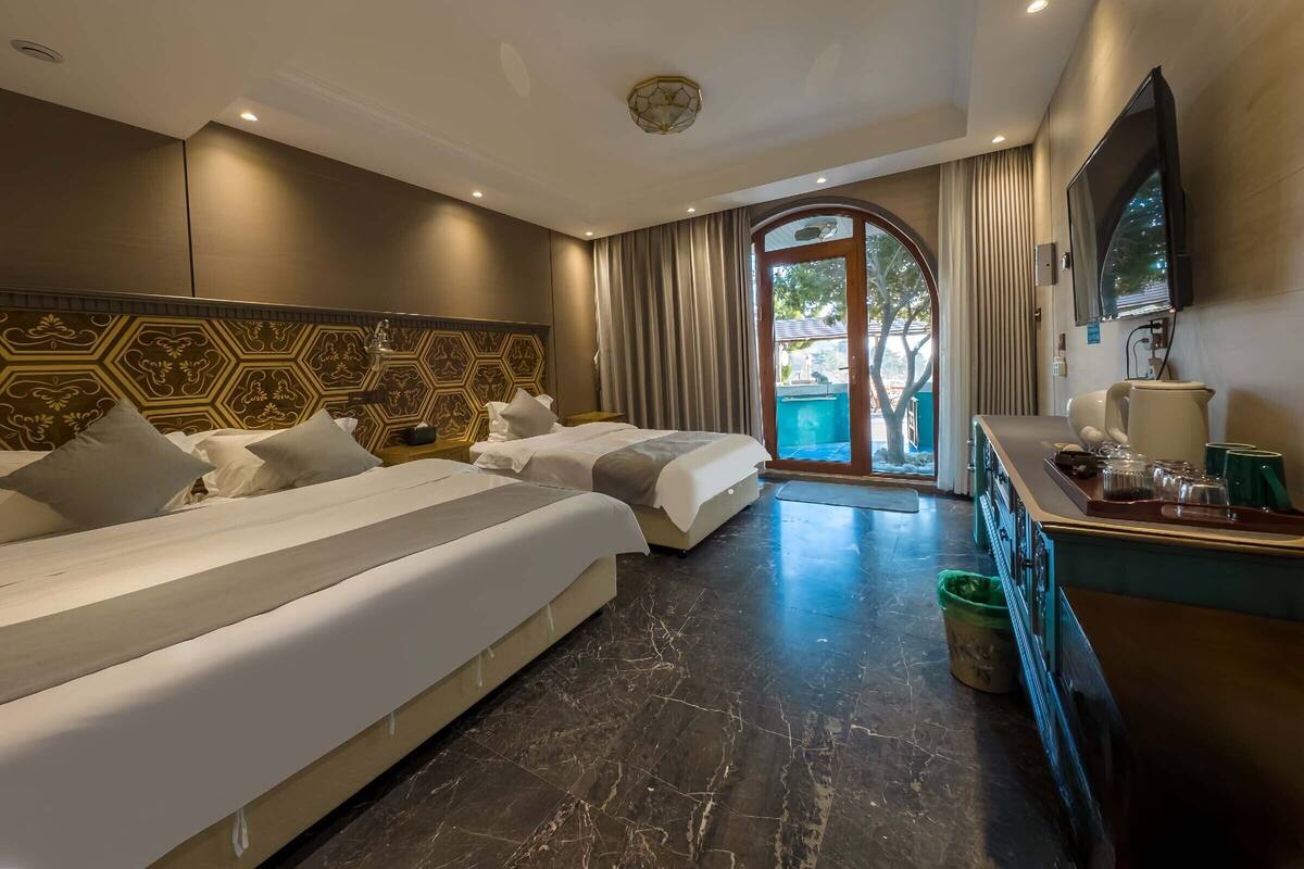 A hotel room with two beds, a TV, a coffee maker, and a view of the outdoors.
