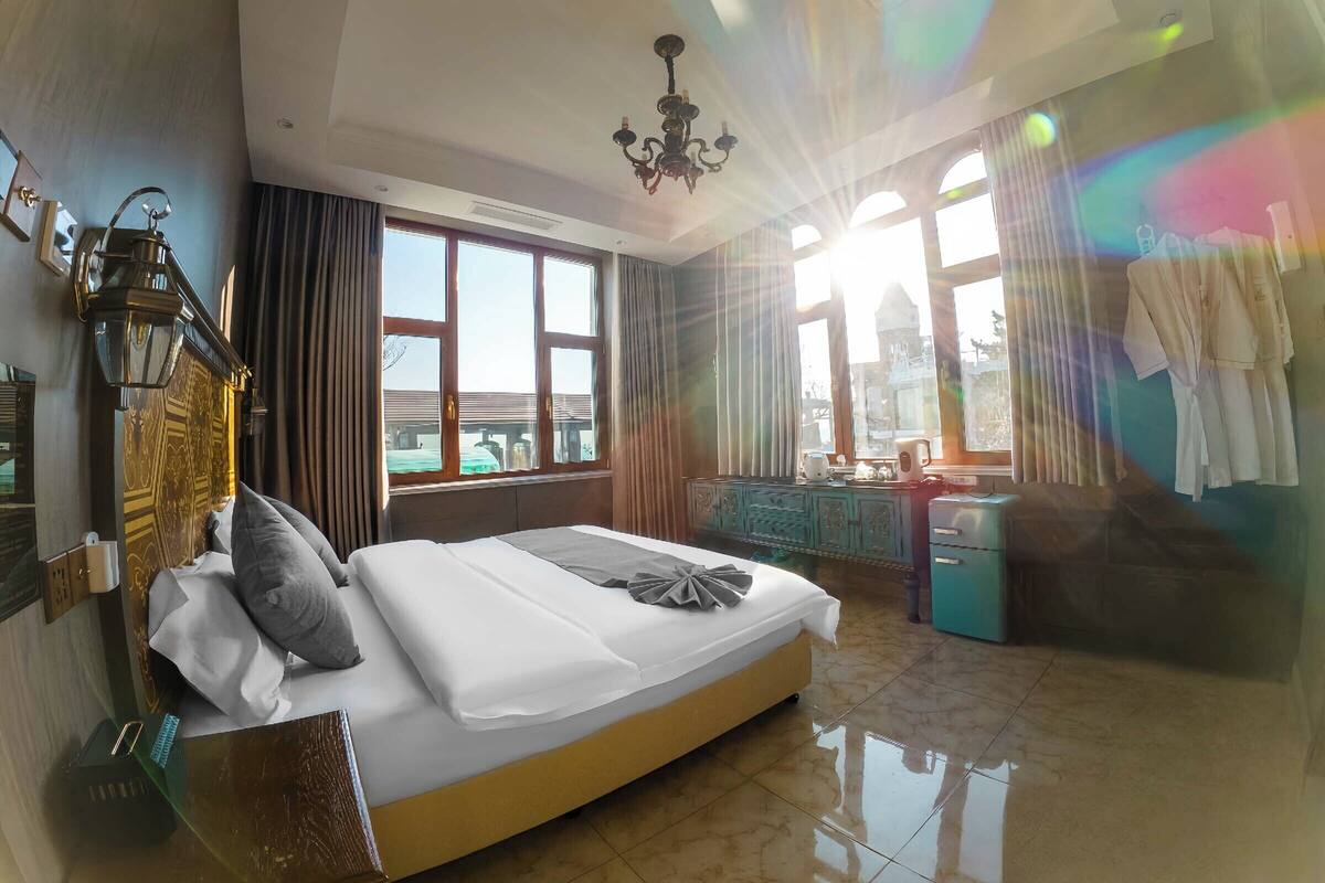 A hotel room with a large bed, a dresser, a vanity with a mirror, and a chandelier.