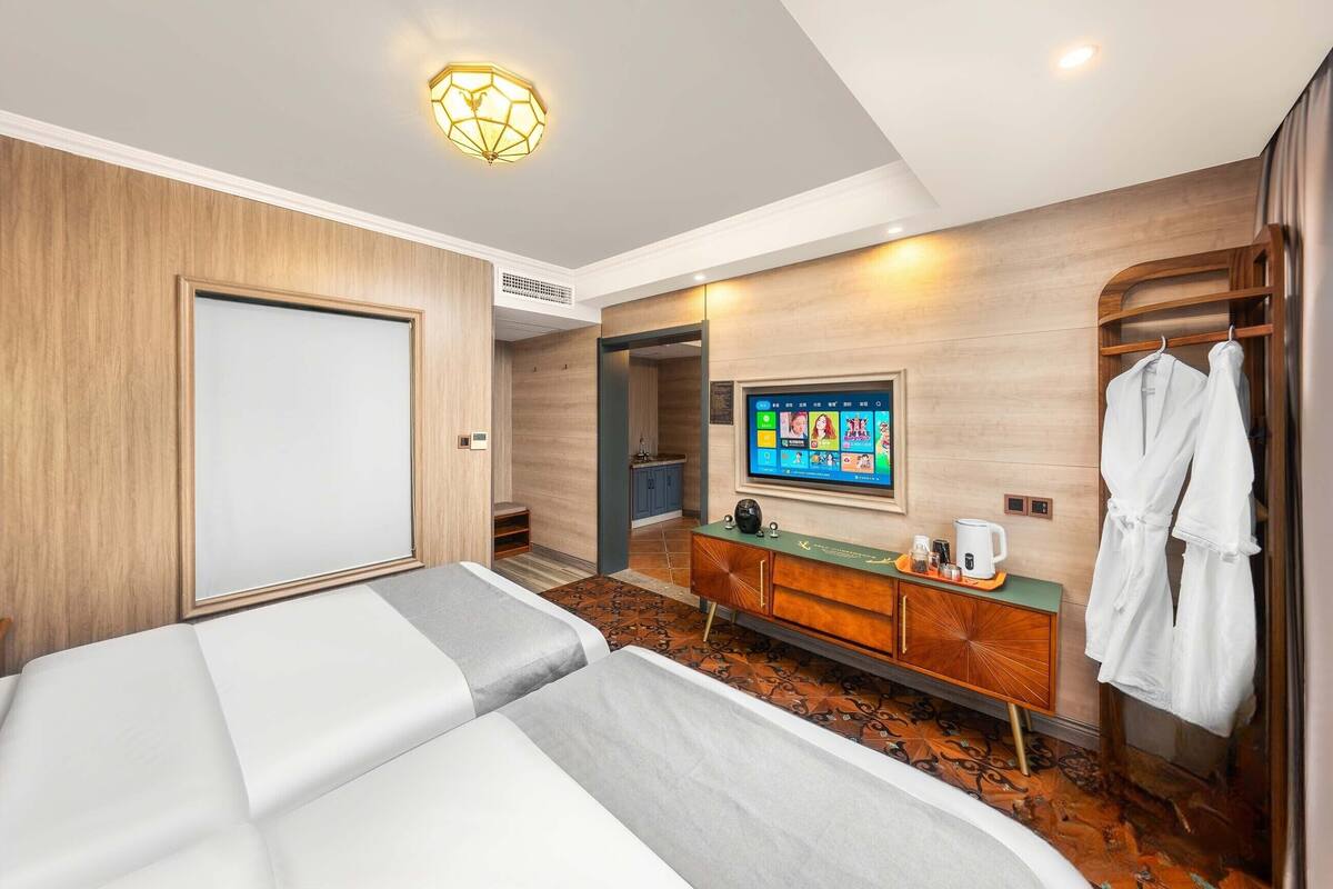 A hotel room with a bed, a TV, a robe, and a small kitchenette.