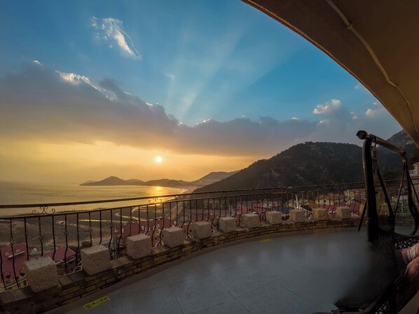 A balcony with a view of the sea and mountains during sunset.