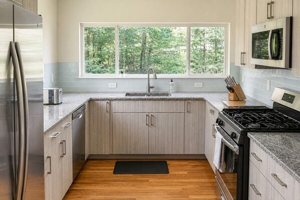 A modern kitchen with a built-in stove, a refrigerator, and a window with a view of trees.