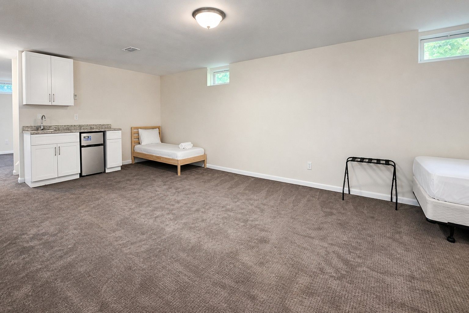 A room with a bed, a small kitchenette, a window, and a mattress on the floor.