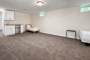 A room with a bed, a small kitchenette, a window, and a mattress on the floor.