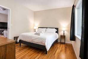 A bedroom with a bed, bedside lamps, a wooden dresser, and a television in the adjacent room.
