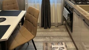 A compact kitchen with a dining area, featuring a modern stove, a small sink, and a dining table with chairs. - G&A Luxe Apartment Central (Târgu Jiu)