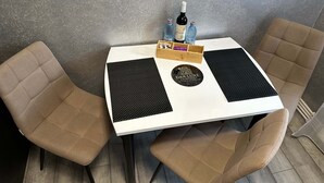 A small table with a white top, two beige chairs, and a black placemat with a logo. - G&A Luxe Apartment Central (Târgu Jiu)