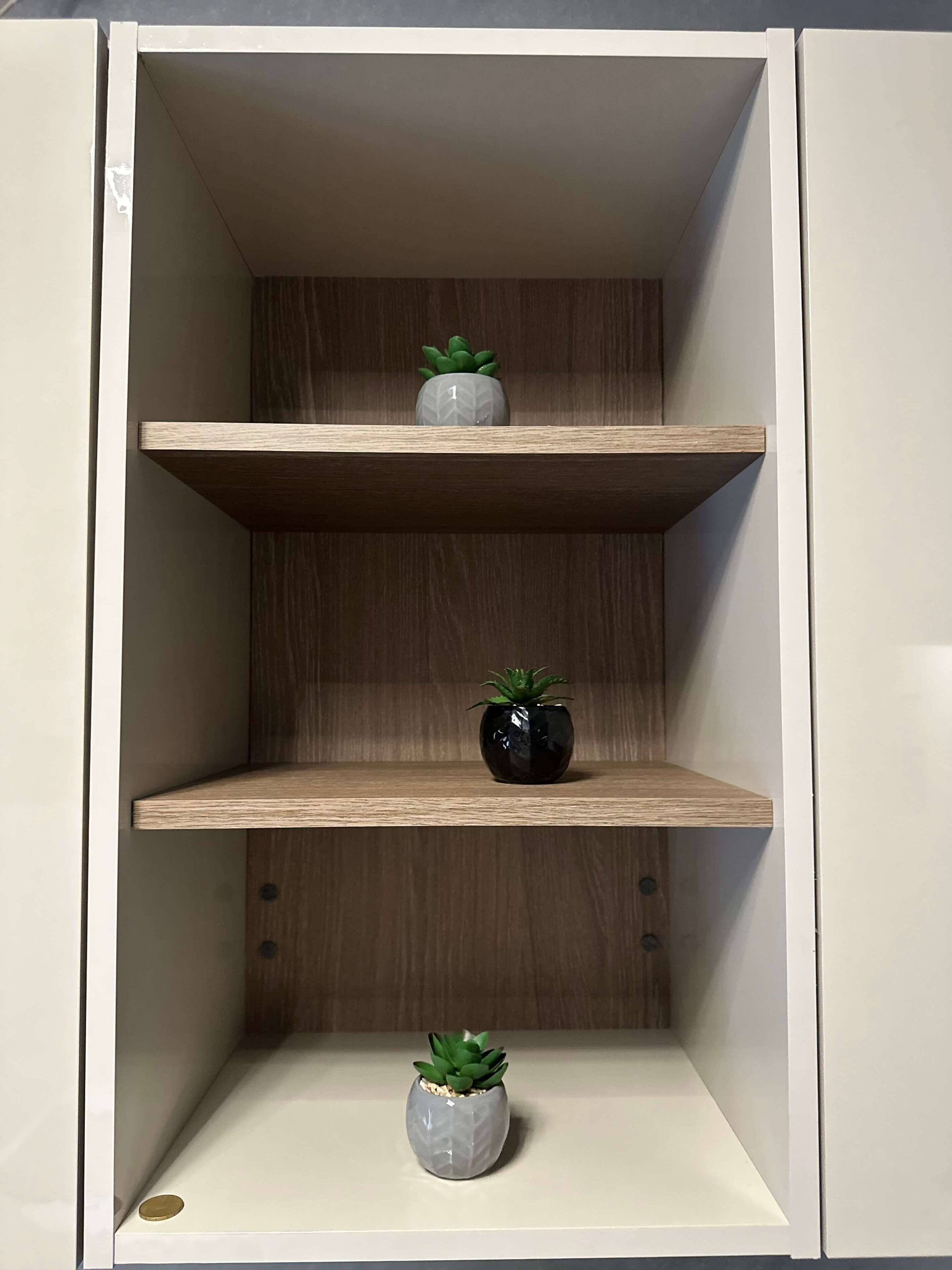 Un mueble blanco con tres estantes, cada uno con una pequeña planta en maceta.
