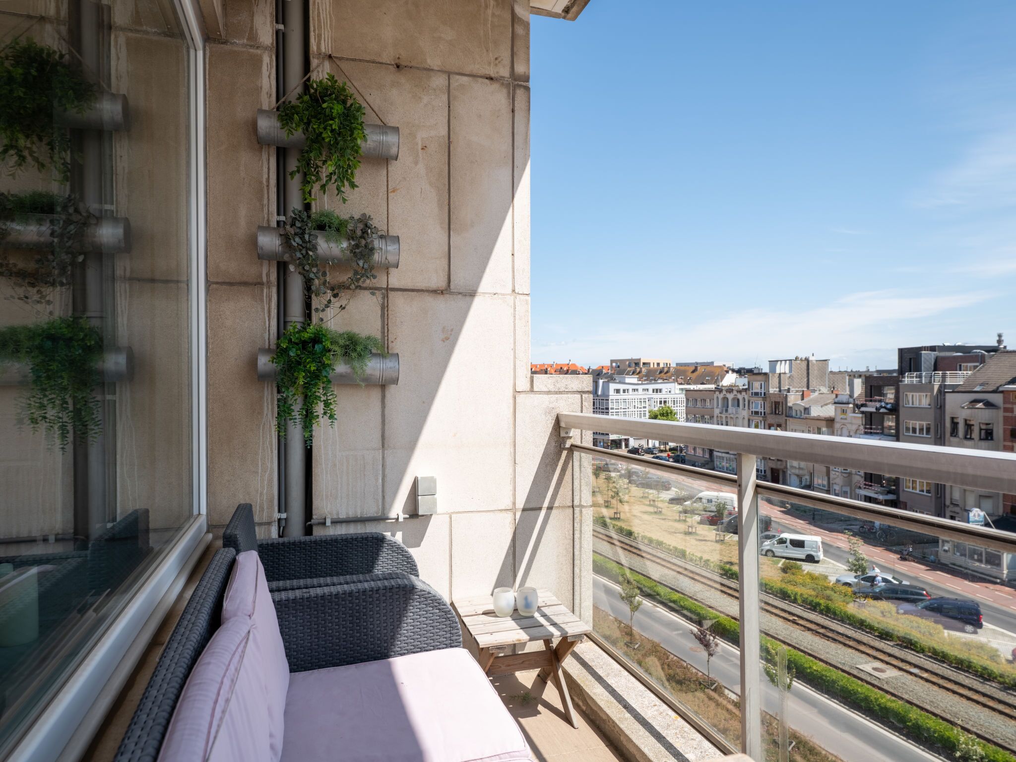 Un balcon avec un canapé, une plante suspendue et une vue sur le paysage urbain.
