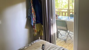Une chambre avec un lit, un téléviseur fixé au mur et une porte-fenêtre coulissante donnant sur un espace extérieur aménagé avec une table et des chaises.