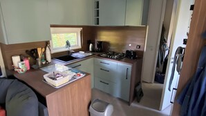Une cuisine compacte équipée d’un évier, d’une cuisinière et de placards. On y trouve également un petit coin salon avec une table et une poubelle.