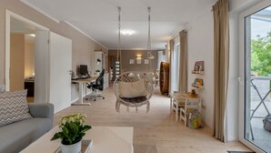 A modern living room with a sofa, a hanging chair, a dining table, and a view through a large window. - Stay in the Heart of Nature (Sankt Wendel)