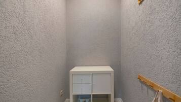 Ein kleiner, weißer Schrank mit zwei Fächern und einem Holzregal darunter, an einer strukturierten Wand.