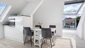 Une cuisine moderne avec un coin repas, des meubles blancs et une lucarne.