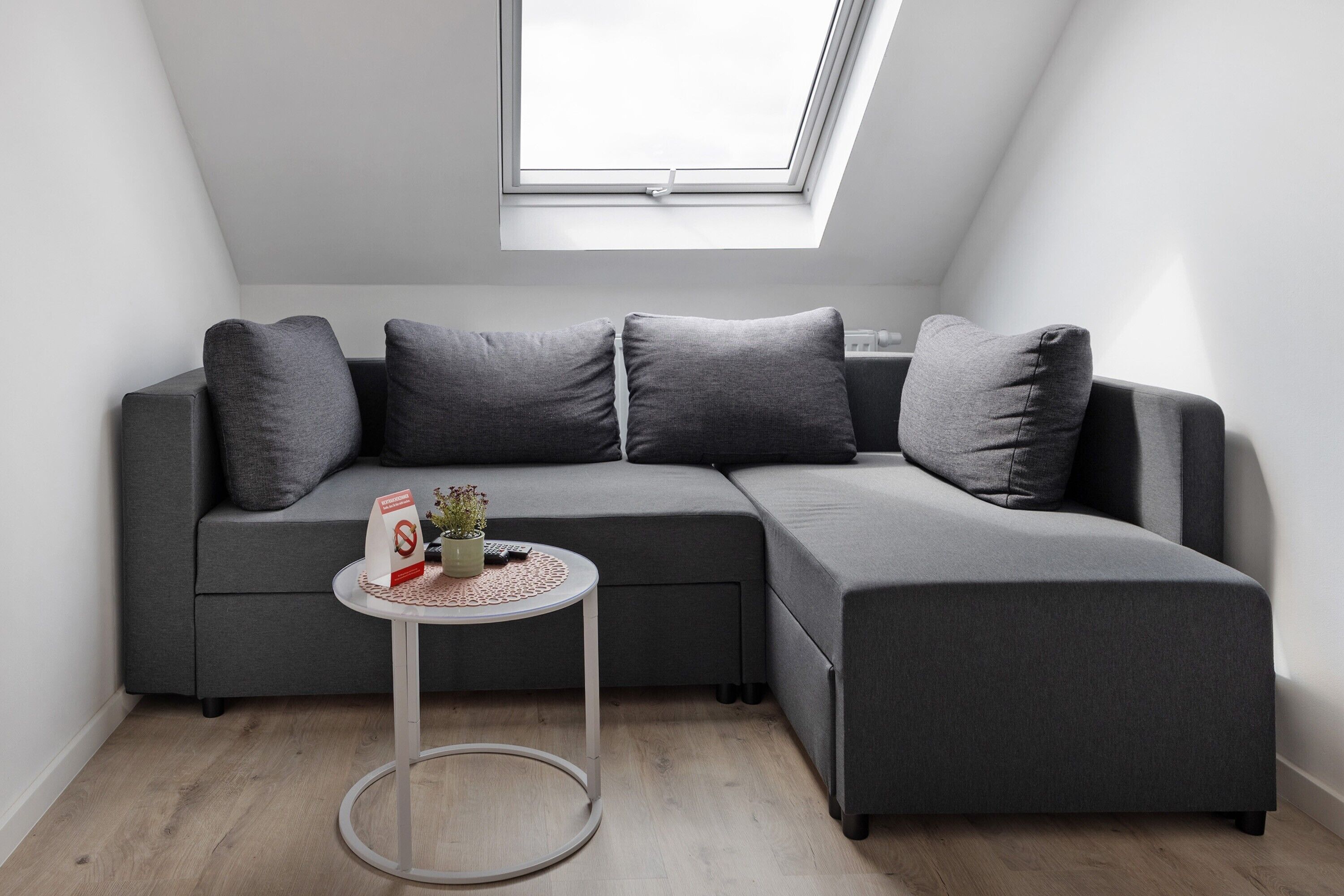A modern room with a grey sectional sofa, a small round table, and a skylight above.