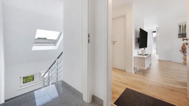 Un intérieur moderne avec un escalier, une lucarne, un téléviseur à écran plat et un plancher en bois.