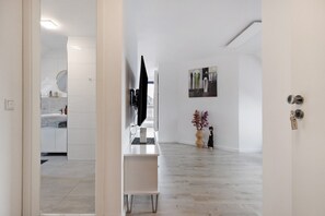 A modern interior with a white bathroom, a flat-screen TV mounted on a cabinet, a painting on the wall, and a keyhole on the door.