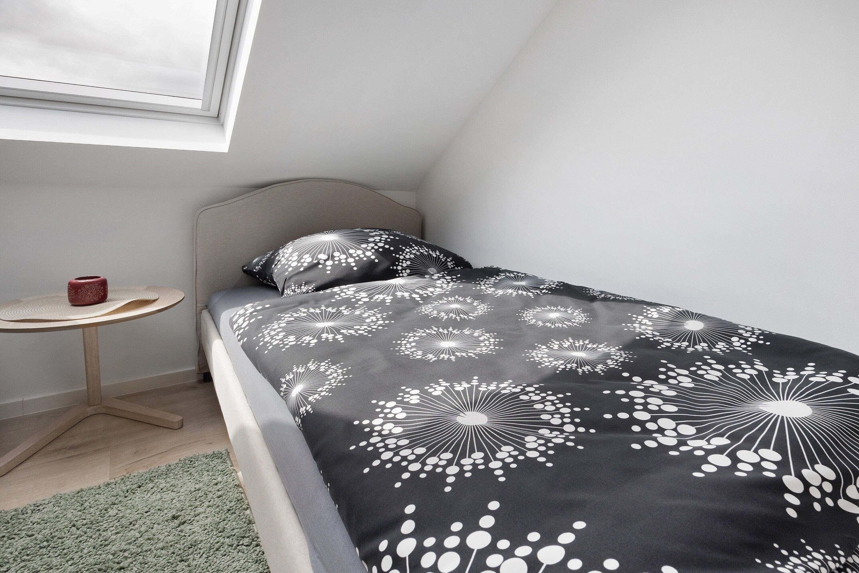 Une chambre avec un lit, une petite table ronde, un tapis vert et une fenêtre.