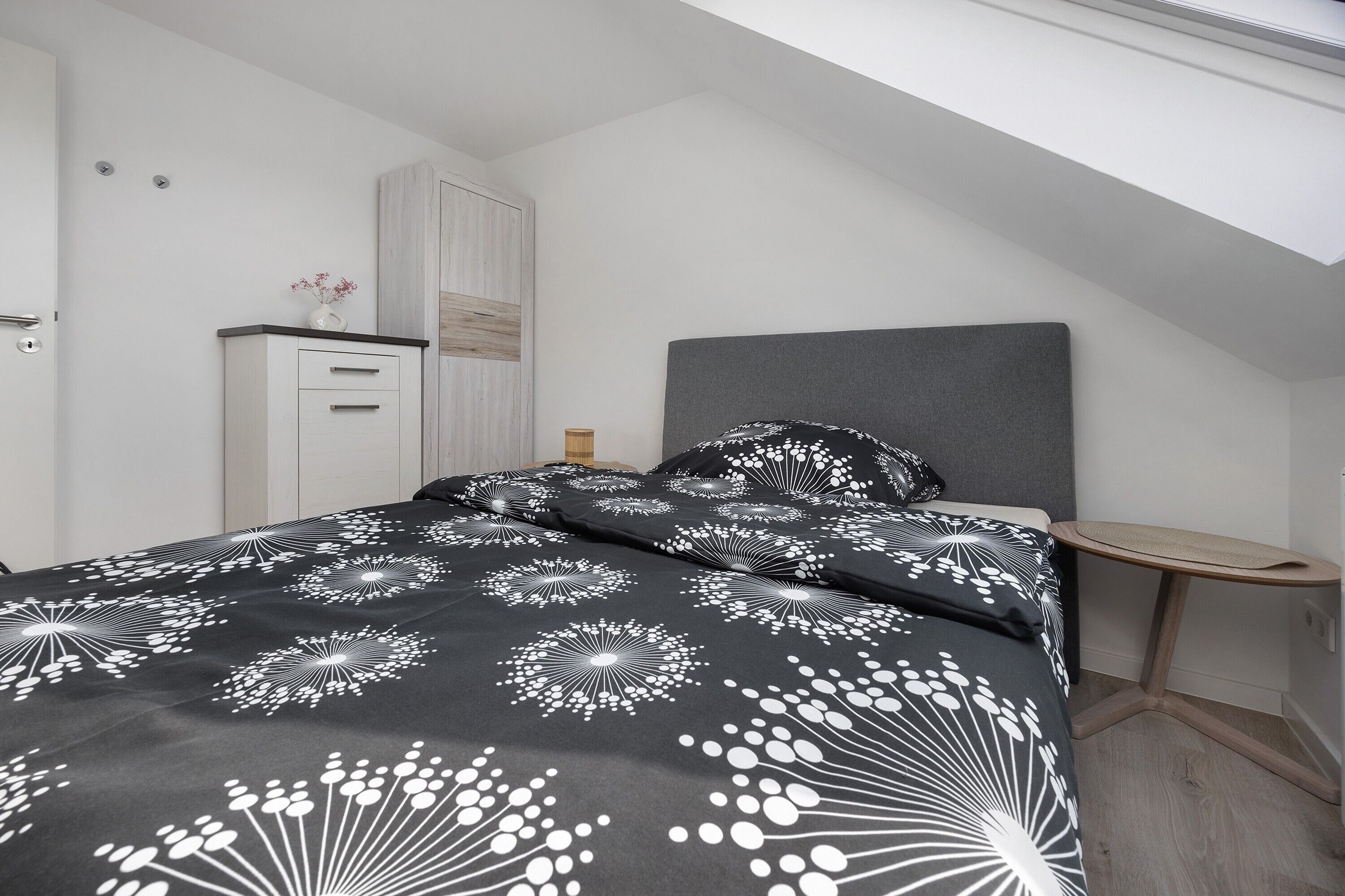Un dormitorio con cama, mesita de noche, armario y tragaluz.