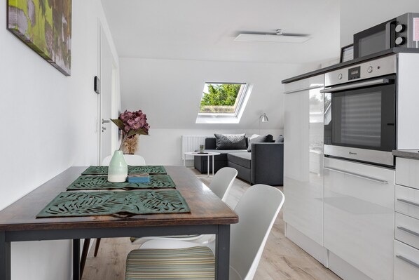 A modern kitchen with a built-in oven, a dining area with a table and chairs, a small sofa, and a skylight.