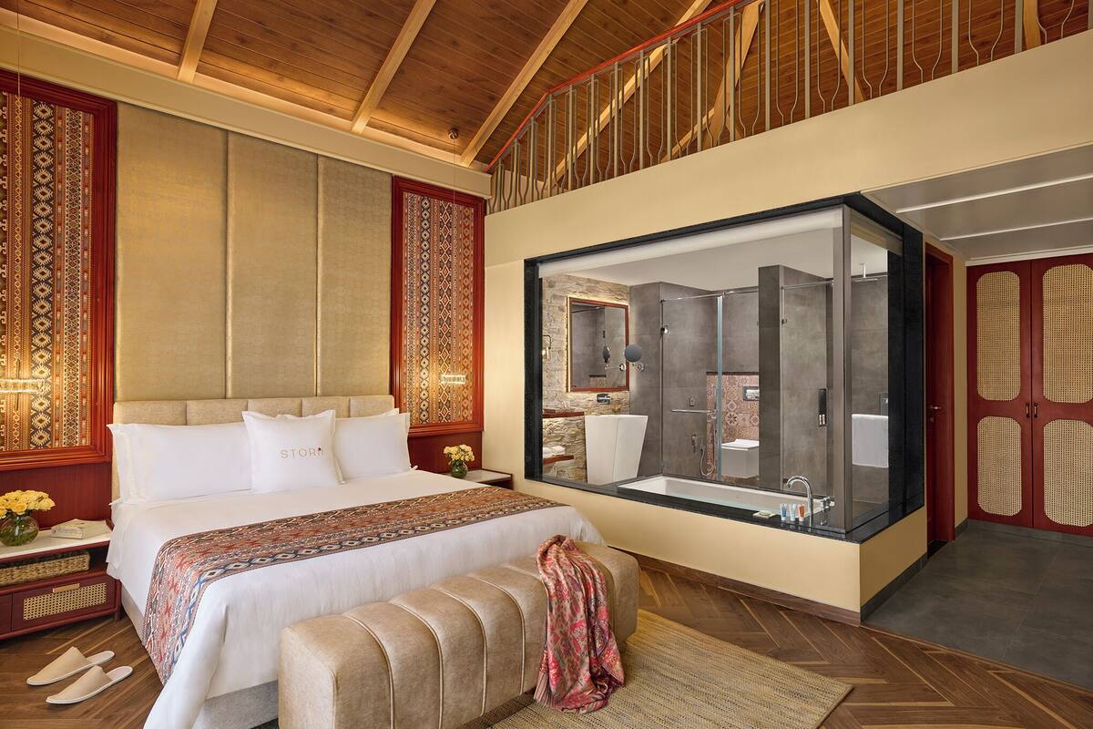 A spacious bedroom with a large bed, a bathroom with a glass-enclosed shower, and a wooden ceiling.