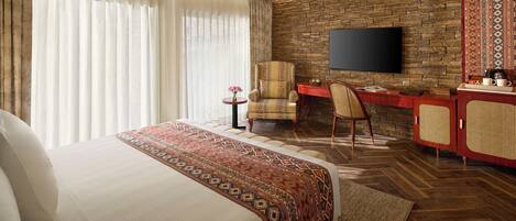 Habitación de hotel con una cama grande, un escritorio con una silla, un televisor montado en una pared de piedra y un armario rojo.
