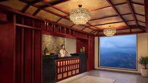 Una zona de recepción con pared de piedra, una recepcionista y un ventanal con vista a la montaña.