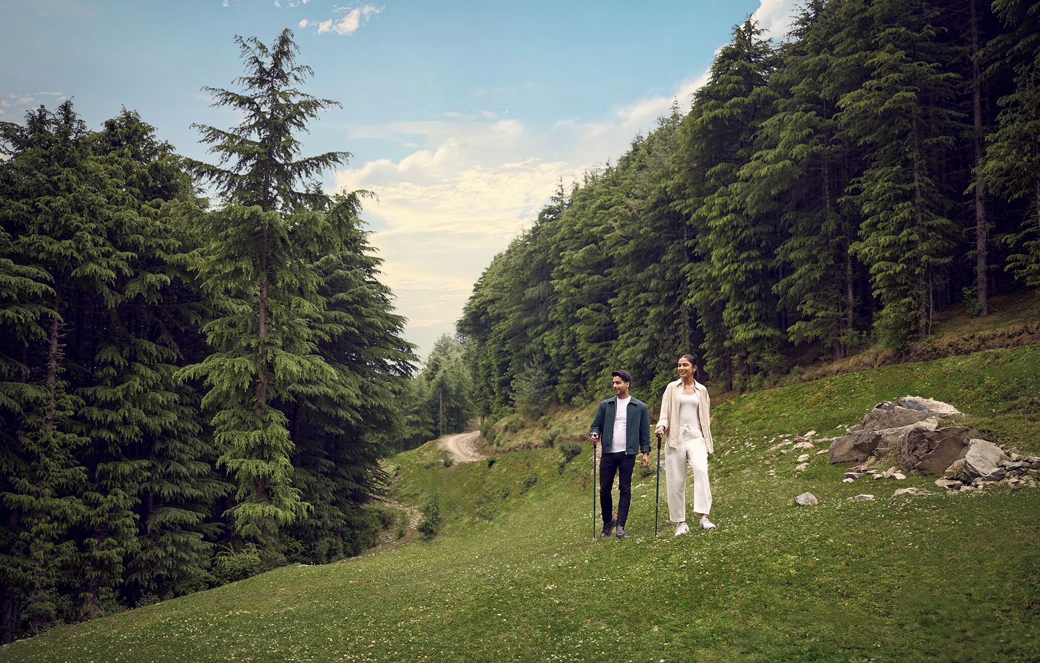 Una coppia cammina su un sentiero erboso, circondata da una fitta foresta.