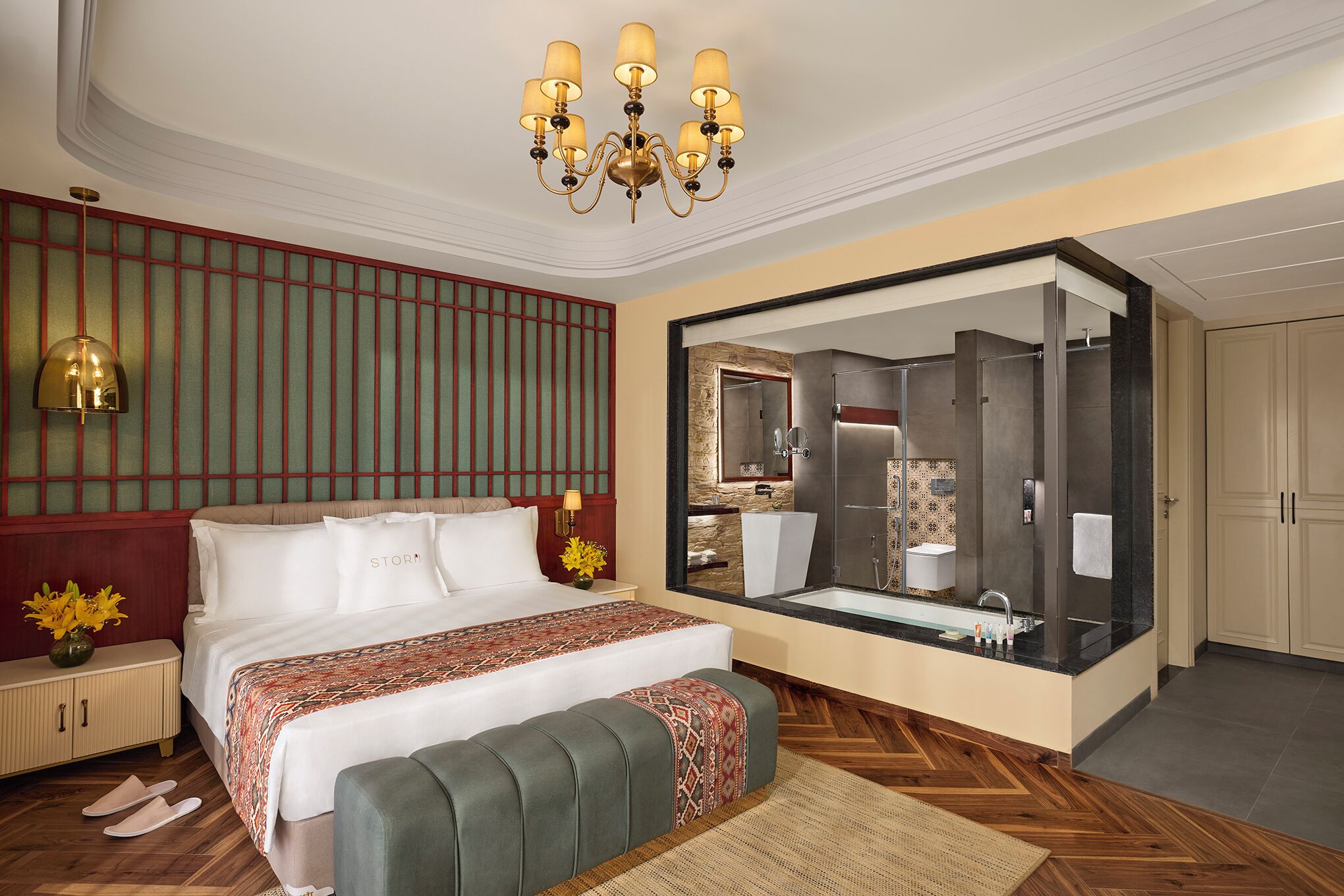A hotel room with a large bed, a sitting area, a bathroom with a large mirror, and a chandelier.