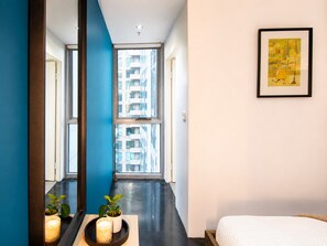 Een moderne hotelkamer met een groot raam, een ingelijste afbeelding aan de muur en een nachtkastje met kaarsen.
